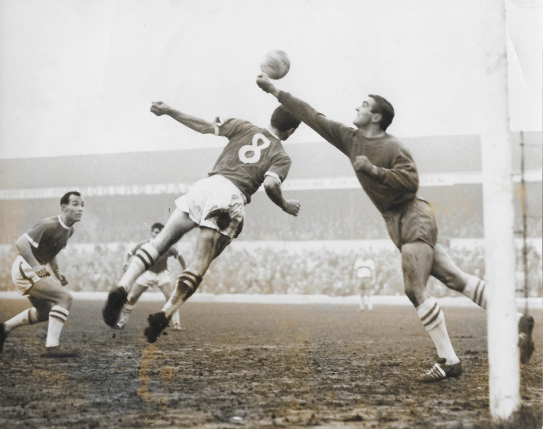 Millwall keeper Reg Davies punches the ball away from the head of 21 year old Arfon Griffiths. Credit: AFCArchive